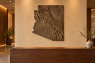 AI-generated commercial concept of a bronze-finished Arizona terrain wall panel behind a hotel reception desk.
